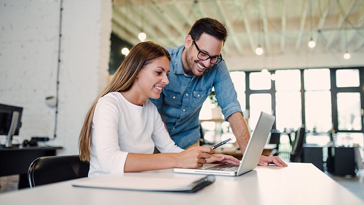 Two colleagues using a laptop and talking in a modern office
