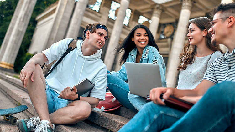 Transforming higher education: four students sitting on steps in conversation around an open laptop