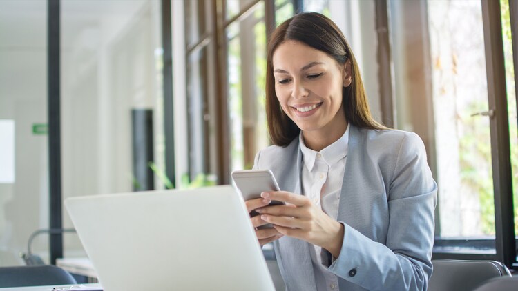 Multifactor authentication (MFA): woman smiling at a phone in her hands in front of an open laptop