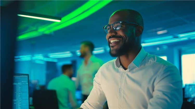 AI platform: Man smiling at a computer screen in a busy office with green and blue lights