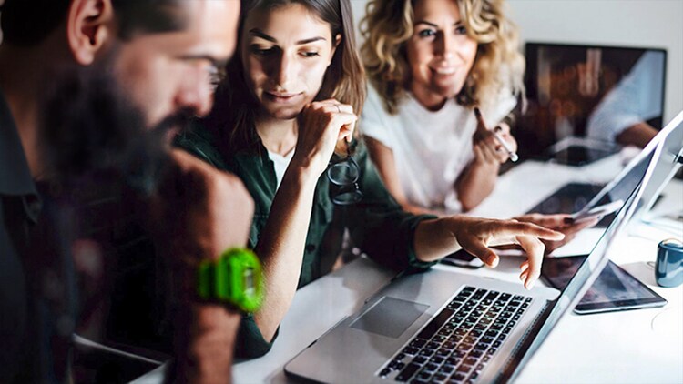 AI innovation: three workers at a conference table looking at an open laptop