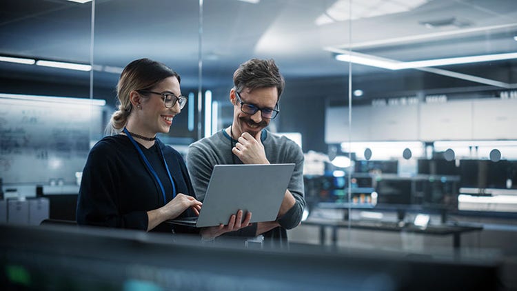 Addressing technical debt: two smiling workers collaborating over a laptop in an office