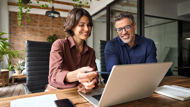 Two people smiling whilst working from a laptop in a bright office