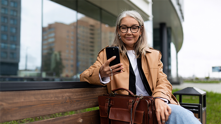 Mature woman sitting outside on a bench looking at a phone in her hand