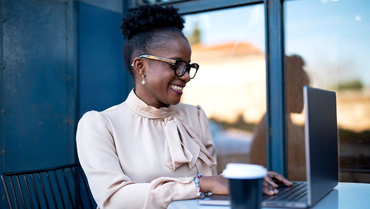 Happy woman drinking coffee while working on a laptop