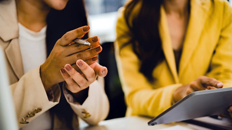 Two coworkers reviewing information together at a desk, one using a tablet.