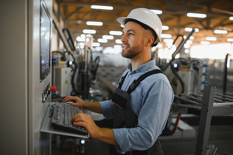 A factory worker wearing a hard hat operates a control panel in a manufacturing hall.